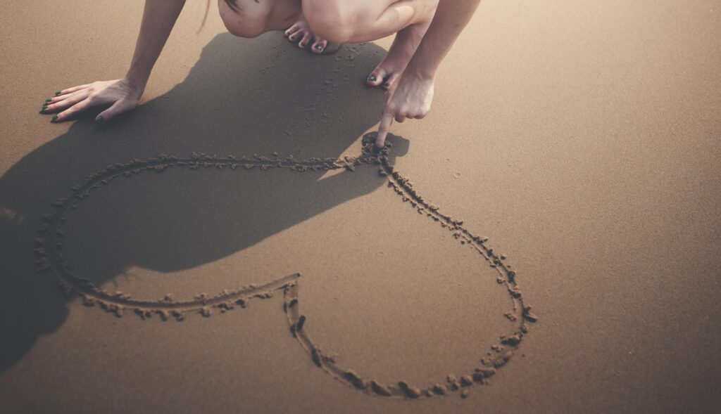 Mulher a desenhar um coração na areia, com o dedo.