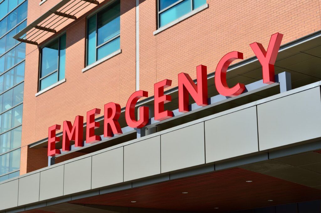 Fachada de um hospital com a palavra "emergência" em letras vermelhas.